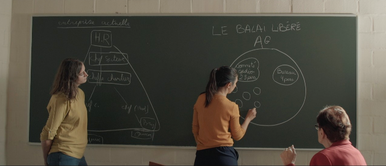 Photo de tournage. Coline entourée de Valérie, actuelle cheffe de chantier à l'UCLouvain, et Julia, ancienne travailleurs au sein du Balai libéré.